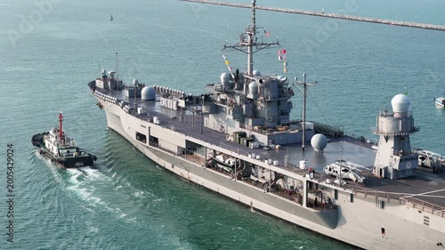 large naval amphibious assault ship being assisted by tugboats in the strategic Strait of Hormuz. Concept of maritime security, naval power projection, and protection of international shipping lanes.