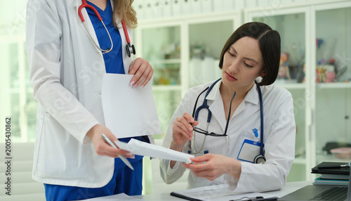 Obraz na plátně Female doctors exchanging and signing forms at desk, decisive handoff moment wit