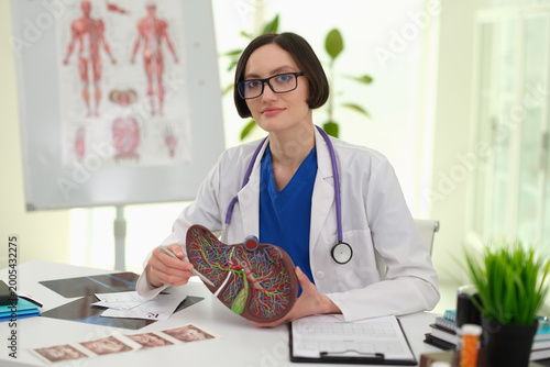 Caucasian female clinician reviewing ultrasound photos next to liver model, explaining imaging findings and care plan to patient