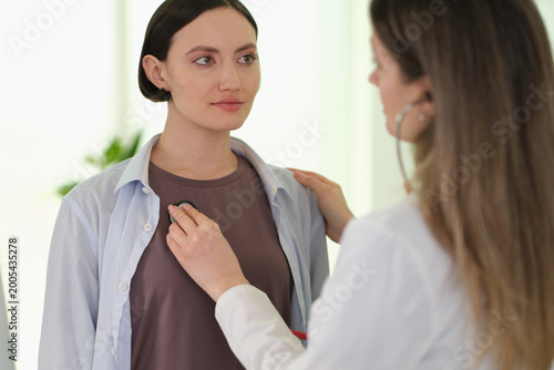 Doctor performing chest auscultation during routine exam patient seated, stethoscope placed on shirt, clinician checking lungs