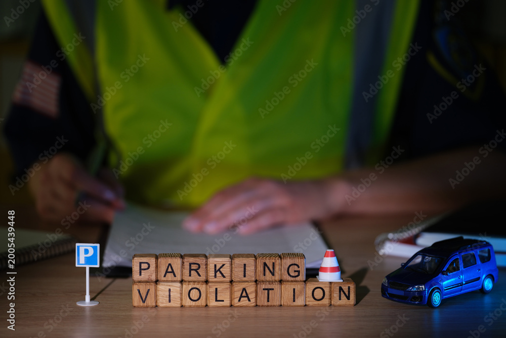 Obraz premium A traffic enforcement officer sits at a desk, writing down parking violations. Wooden blocks spell out PARKING VIOLATION, beside a small traffic cone and a toy car, creating a serious atmosphere.