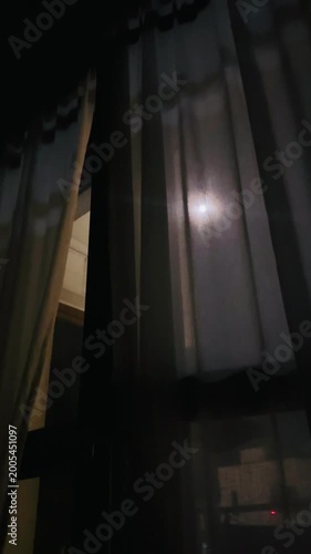 Full moon shining through sheer curtains in a darkened room  