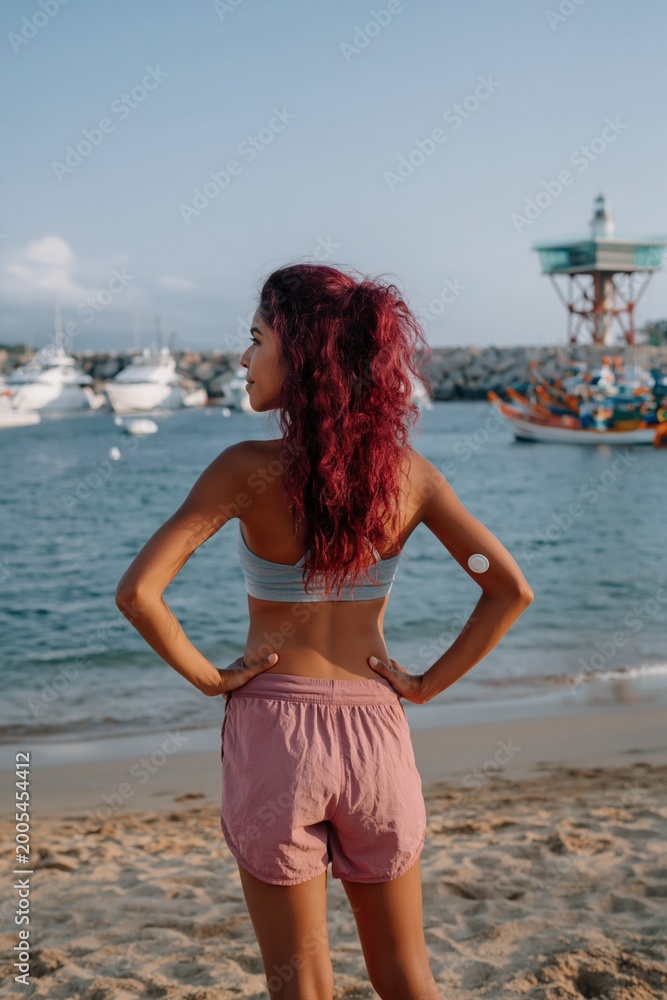 Fototapeta premium Young woman standing facing marina on sandy beach waterfront