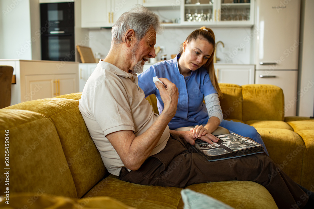 Obraz premium Caregiver comforting senior man while looking at a photo album at home