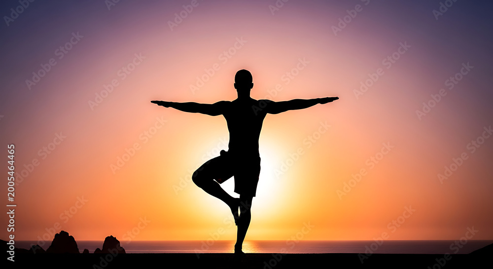 Fototapeta premium Man doing yoga tree pose silhouette at sunset beach