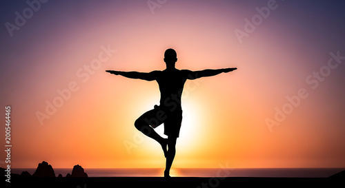 Man doing yoga tree pose silhouette at sunset beach