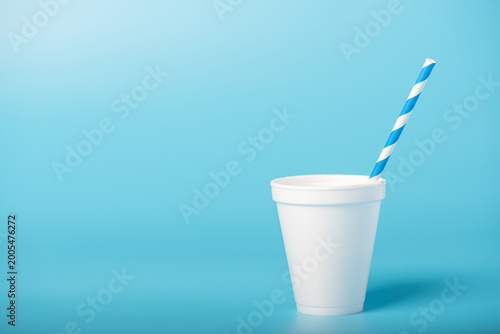 Photos A white cup with straws, a white cup with blue and white straws on a blue background, selective focus