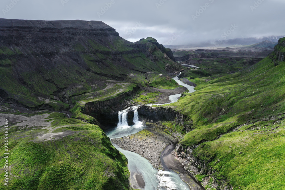 Fototapeta premium Aerial top-down view of twin waterfalls cascading through mossy tundra, Umnak Island, Aleutian Islands, Alaska