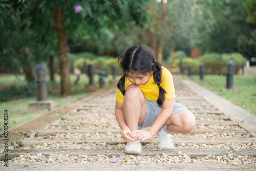 Young girl squatting on gravel path in park, looking for small stones, wearing yellow shirt and gray shorts, peaceful outdoor environment with greenery