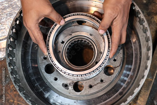 A close-up shot of a mechanic's hands carefully installing a heavy-duty tapered roller bearing into a precision-machined metal transmission component during a mechanical repair process.