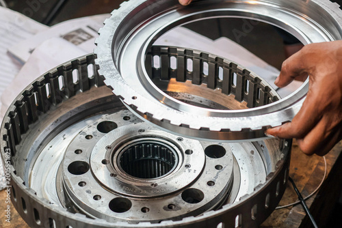 Quadro em tela A close up shot of a technician's hands carefully aligning and inserting a large circular metallic piston component into a heavy duty transmission gearbox during assembly