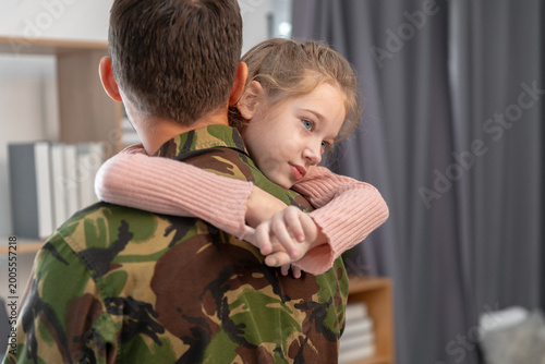Billede på lærred girl hugging military father at home after reunion, emotional family moment with soldier in camouflage uniform, love, support, bonding, parenting and homecoming concept