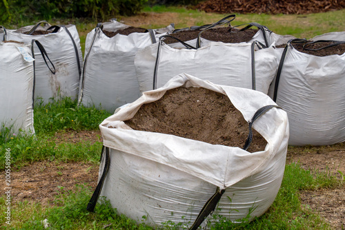 Multiple large white bulk bags filled with brown soil for gardening and construction use