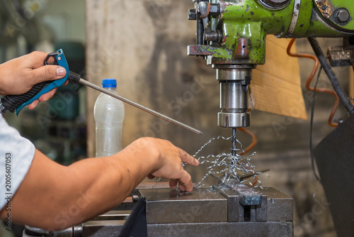 Skilled machine operator clearing spiral metal chips from an NC milling machine during drilling process.