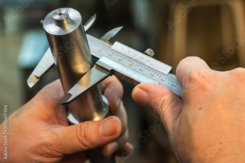 Billede på lærred Skilled machine operator measuring the outside diameter of a metal shaft using a vernier caliper