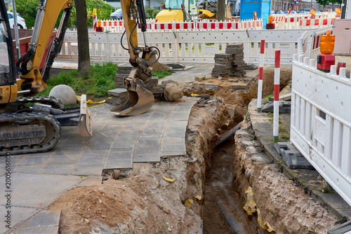 Photography Excavator working on a narrow trench for utility pipelines on a city sidewalk