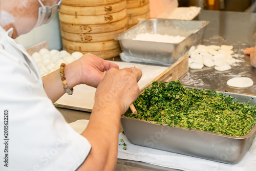 Картината върху платно In a semi-open kitchen, chefs carefully prepare xiaolongbao by flattening dough into thin wrappers and filling them with minced pork and chives