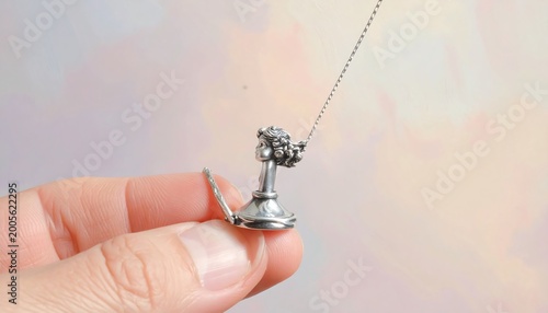 A hand holding a small silver pendant on a chain