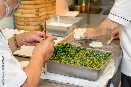 Quadro su tela In a semi-open kitchen, chefs carefully prepare xiaolongbao by flattening dough into thin wrappers and filling them with minced pork and chives