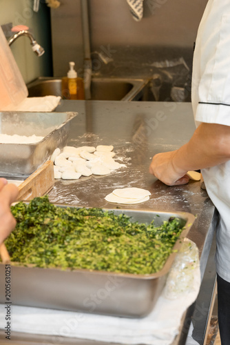 Photography In a semi-open kitchen, chefs carefully prepare xiaolongbao by flattening dough into thin wrappers and filling them with minced pork and chives