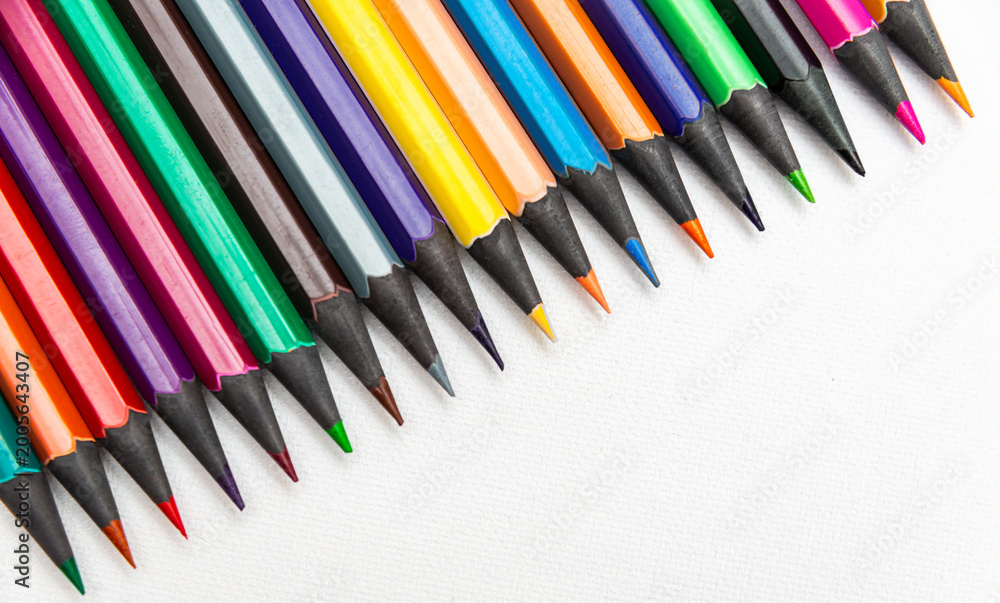 Fototapeta premium Colorful pencils arranged in a straight line on a white background during a daylight setting