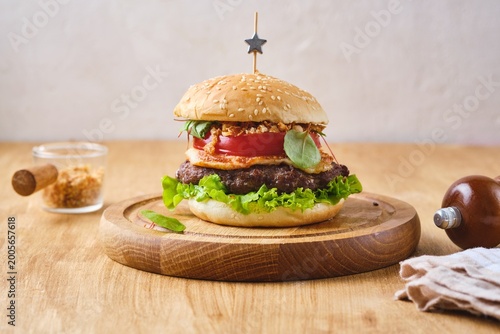 Tableau sur toile A ready-made burger with a beef patty, melted cheese, crispy onions, tomato, and lettuce on a wooden board against a wooden background
