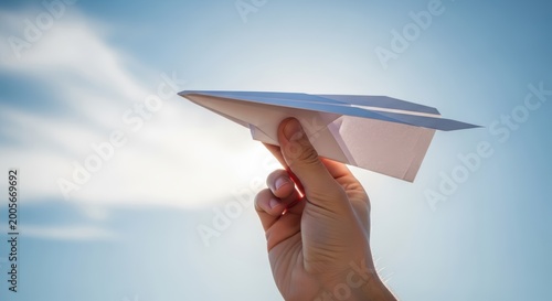 Hand holding paper airplane against sunny blue sky