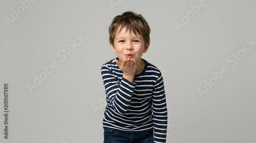 A young boy in a striped shirt blowing a kiss with a grey background, conveying affection and charm