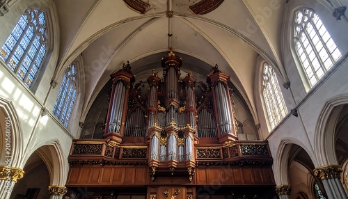 Interior view of a church, featuring a grand pipe organ situated above the altar with stained-glass windows