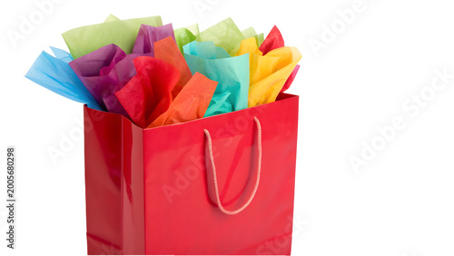 Vibrant red shopping bag overflowing with colorful tissue paper on white background