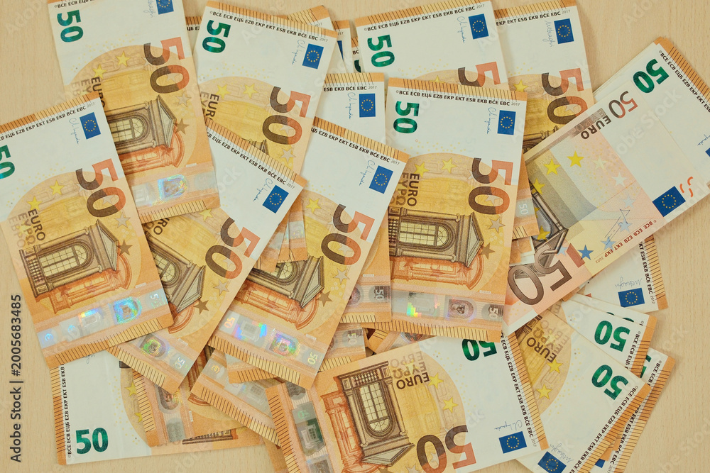 Obraz premium Fifty euro banknotes are scattered across a wooden surface in a layered cash pattern. Mid value currency concept for payment, budgeting, retail and consumer finance.