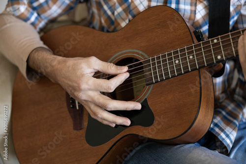 Fotografia Male guitarist strumming acoustic guitar strings with focused hands, creating me