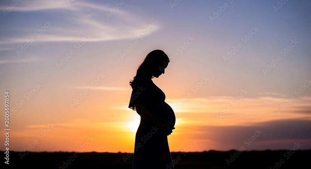 Fototapeta premium Pregnant woman standing in profile against vibrant sunset sky with wispy clouds and serene landscape