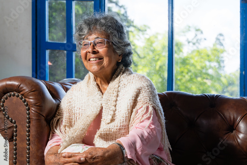 Fotografia Afro-Colombian elderly woman with curly gray hair and glasses sitting on a brown
