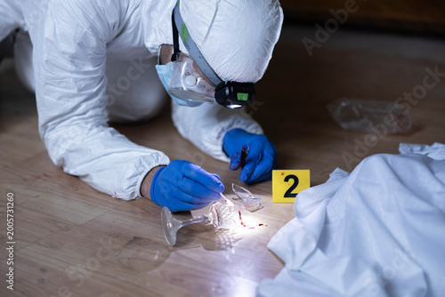 Obraz na płótnie Wearing protective gear, a forensic investigator examines broken glass and blood
