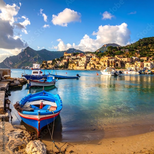 Scenic coastal view showcasing a harbor with boats, charming buildings, and a backdrop of mountains under a bright blue sky