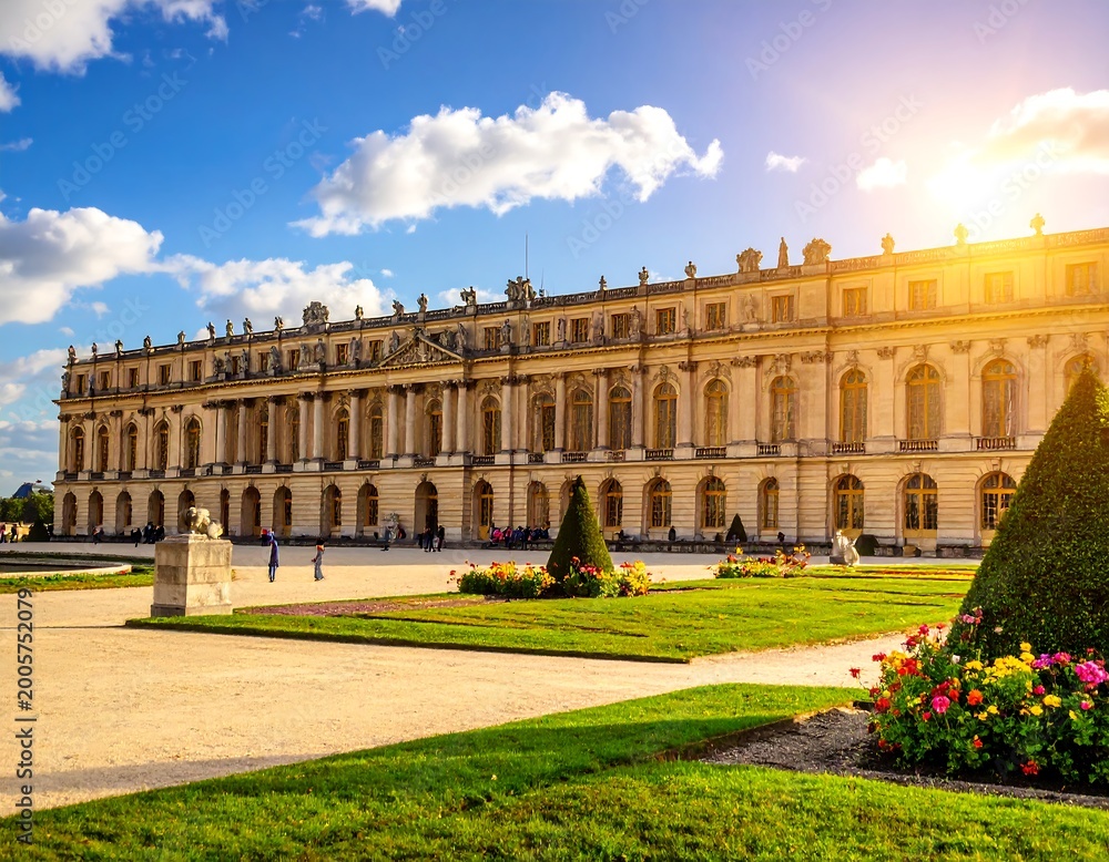 Fototapeta premium Large, stately structure with symmetrical design, adorned with many windows and intricate details. Well-manicured gardens and blue sky