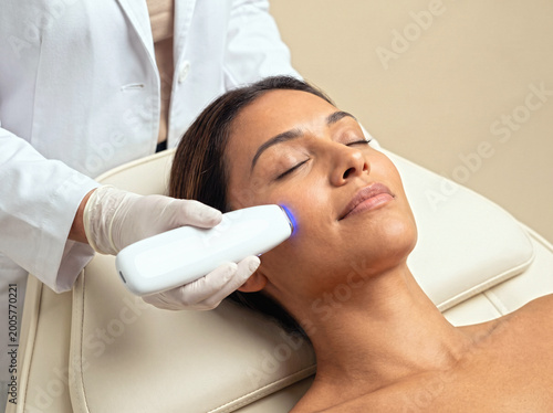 Dermatologist performing cosmetic laser lifting and collagen boost therapy on patient in modern dermatology center