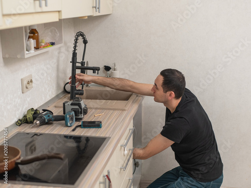 A plumber is replacing a faucet in the kitchen.