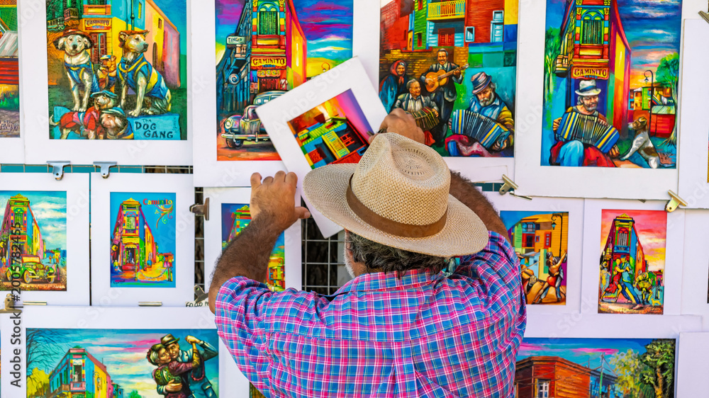 Naklejka premium Local artist arranging vibrant colorful paintings of Caminito in the La Boca district oaf Buenos Aires, Argentina