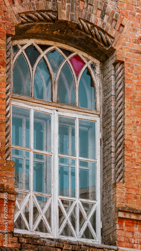 Ornate gothic arched window with red glass detail in old brick wall 