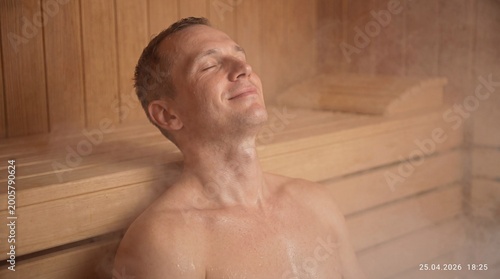 Man relaxing in wooden sauna, eyes closed, enjoying steam, smiling, wellness, relaxation, interior, spa, rest.