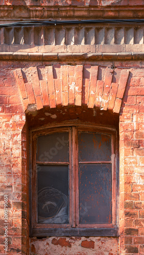 Peeling arched window in warm sunlit red brick wall close up 