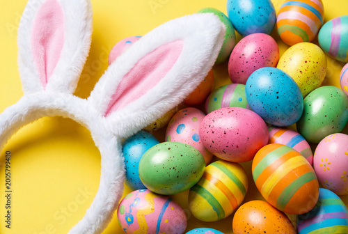 Bunny ears headband and vibrantly colored easter eggs on yellow background