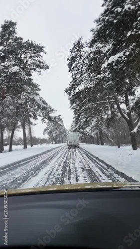 Driving on a snowy road through a winter forest. First-person perspective from a car dashboard driving on an icy, snow-covered asphalt road. Winter woodland landscape with tall trees and overcast sky.