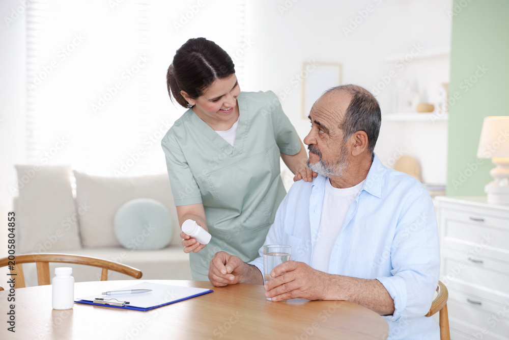 Obraz premium Smiling care worker working with senior man at wooden table at nursing home