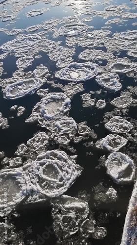 Pancake ice floes on the Warta river in January. High-angle view of circular pancake ice formations floating on the dark waters of the Warta river during a sunny winter day.