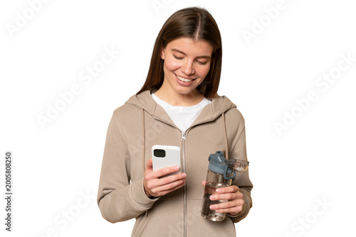 Sporty woman in hoodie having rest after fitness training with bottle of water and phone in hands