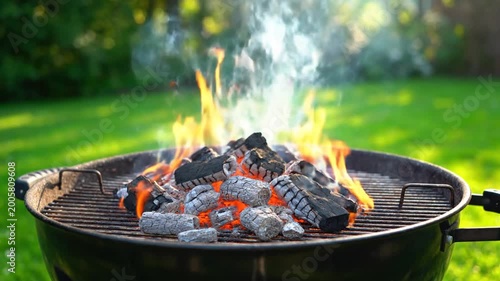 Burning charcoal in a round grill with flames and bright green grass background