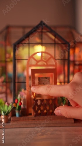 A cozy interior view of a handmade miniature flower shop diorama. Features tiny furniture, paper plants, and warm lighting, showcasing the intricate details of a creative DIY dollhouse room box.